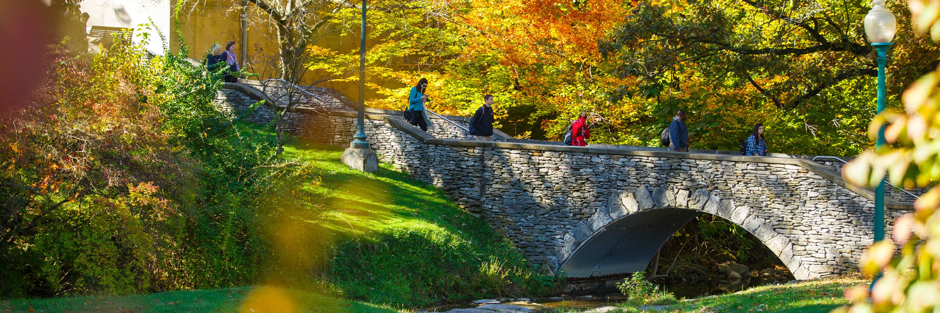 Students crossing a bridge over the Jordan River on the IUB campus