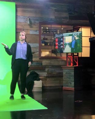 Sarah McCorkle standing in front of a green screen to report on the weather