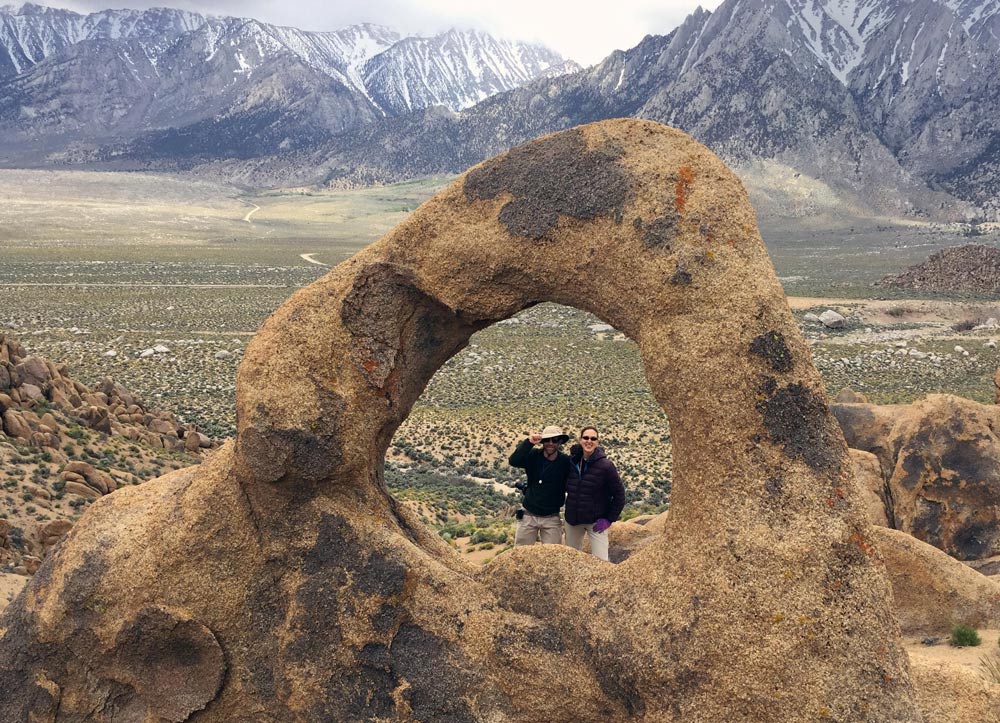 Two people smiling at the camera through a hole in a unique rock formation