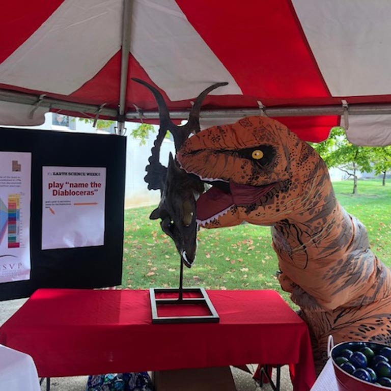 Department's T. Rex mascot jokingly gnawing on a fossil