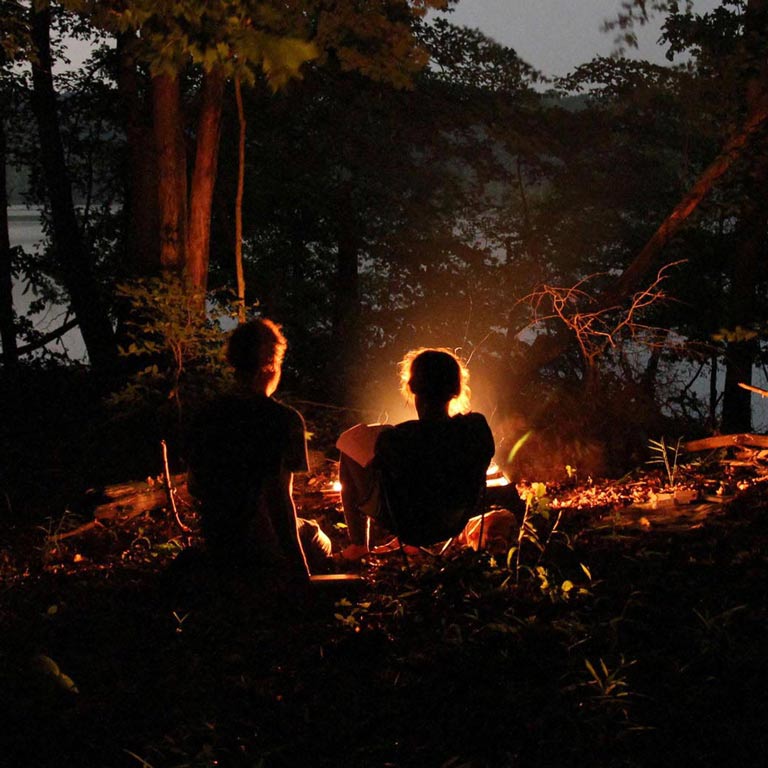 Two people sitting out by a fire in the woods