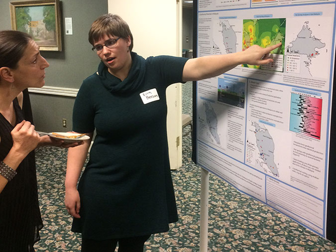 Student pointing at research poster and explaining to another