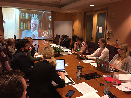 People in a conference room with computers listening to a conference on a projector screen